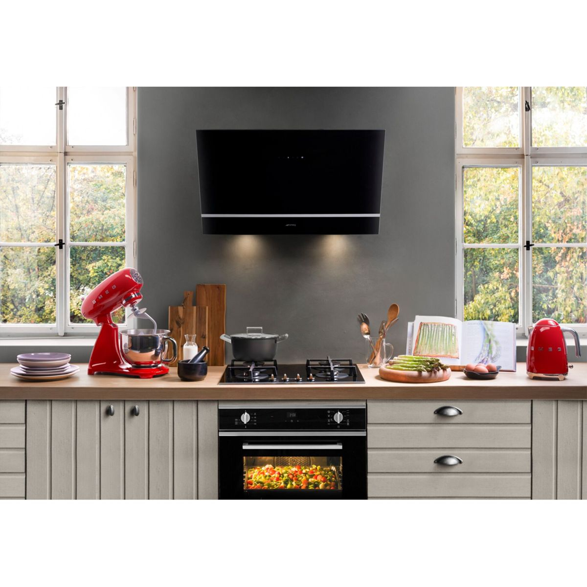 Een keuken scène met een rode mixer, een zwart fornuis, een oven met eten en een zwarte afzuigkap. Ramen zorgen voor natuurlijk licht.