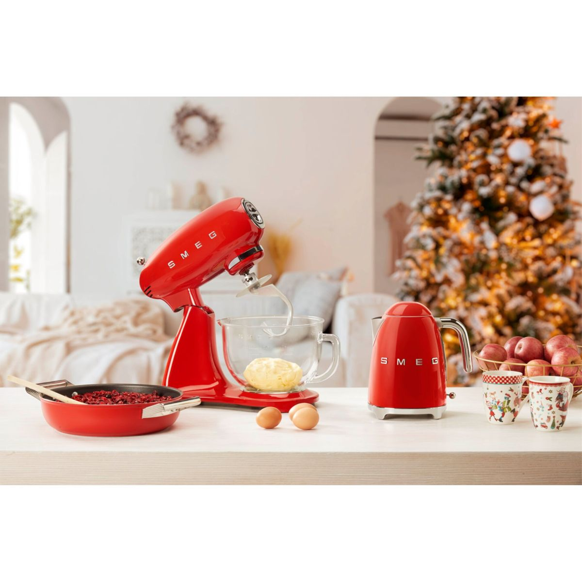 Een rode mixer, waterkoker en pan met ingrediënten op een tafel. Een kerstboom op de achtergrond.