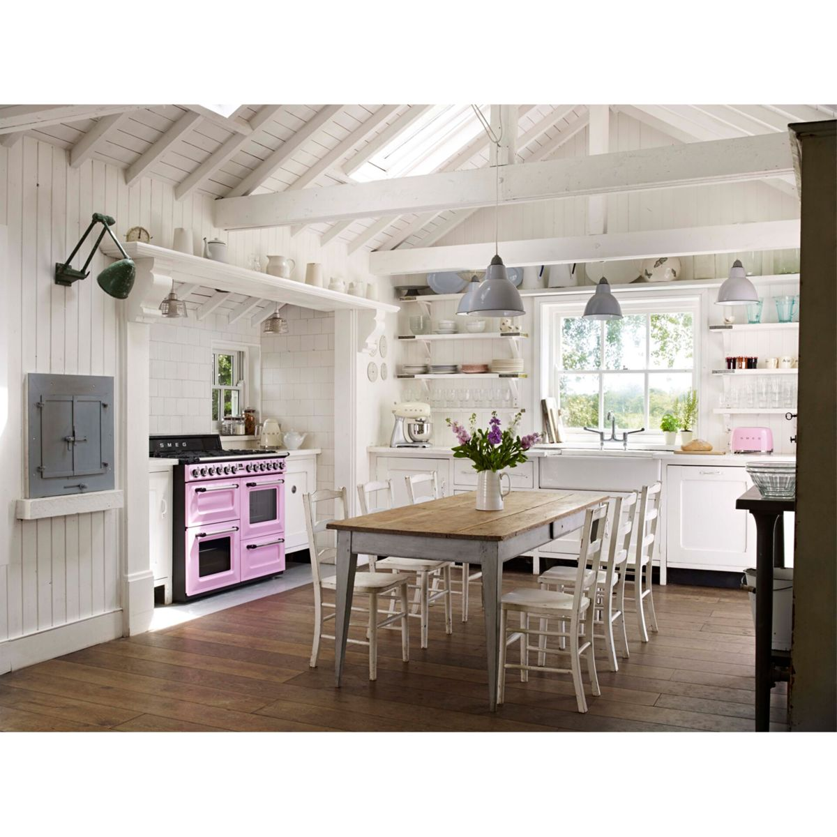 Jasna kuchnia z różowym piekarnikiem, drewnianym stołem, białymi krzesłami i oknem z widokiem.