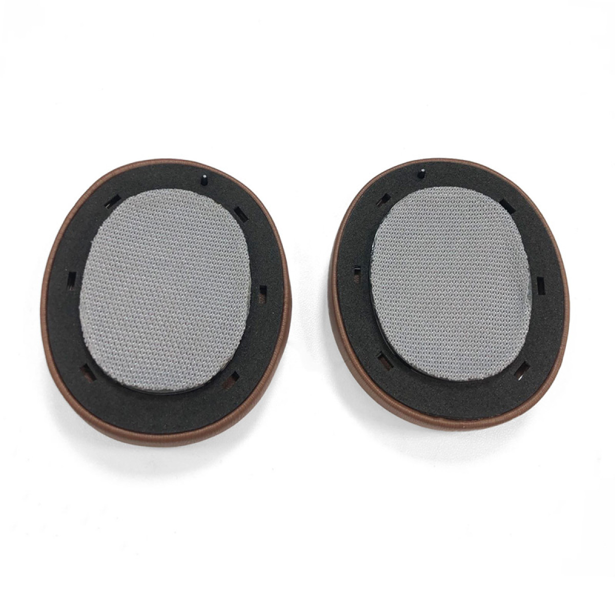 Twee oorkussens voor hoofdtelefoons. Bruine buitenringen, zwarte binnenringen, grijze mesh-middens. Witte achtergrond.