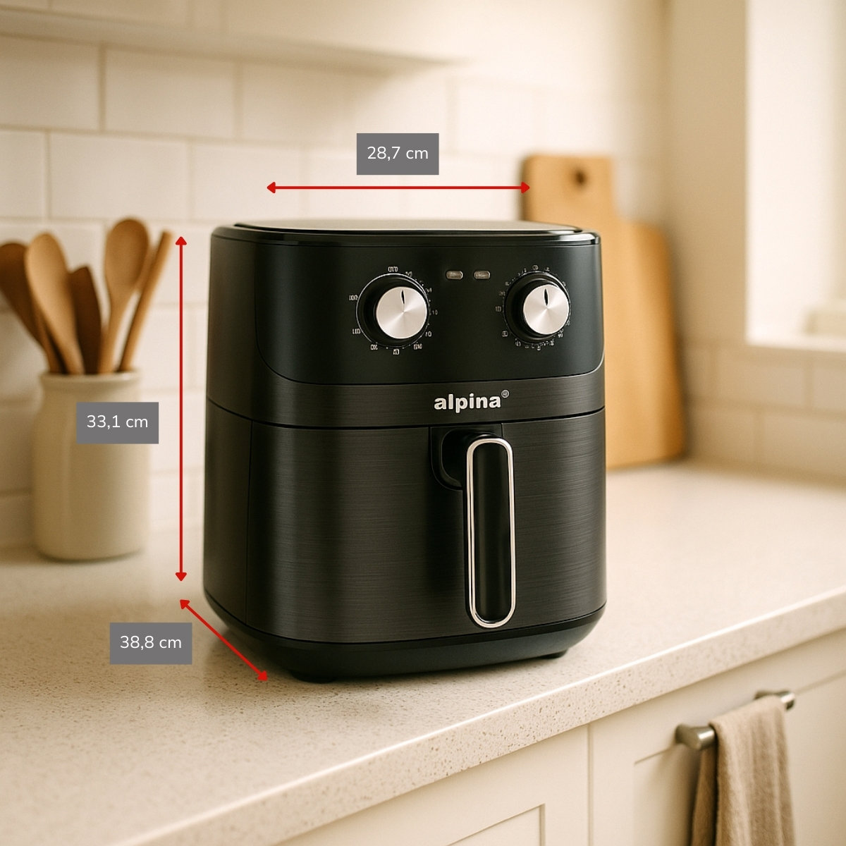 Zwarte airfryer op een aanrecht. Het heeft knoppen, een handvat en afmetingen. Houten lepels en snijplank op de achtergrond.