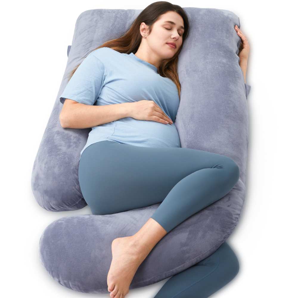 Zwangere vrouw die slaapt op een groot grijs kussen. Ze draagt ​​een blauwe legging en een shirt. De achtergrond is wit.