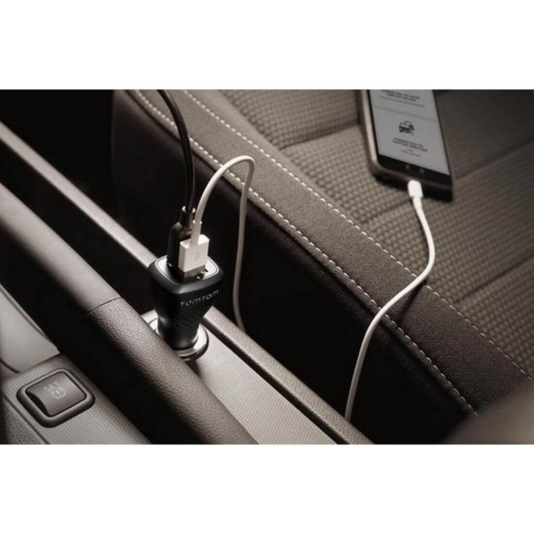 Interno auto. Un telefono si carica tramite un cavo bianco. Un caricatore per auto TomTom nero è nella presa.