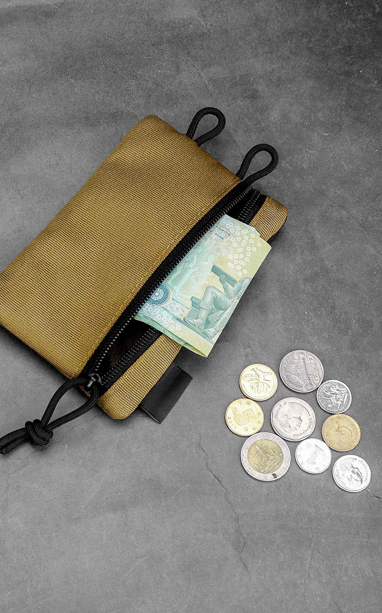 Eine braune Tasche mit Reißverschluss, die einen Geldschein enthält. Münzen sind auf einer grauen Oberfläche verstreut.