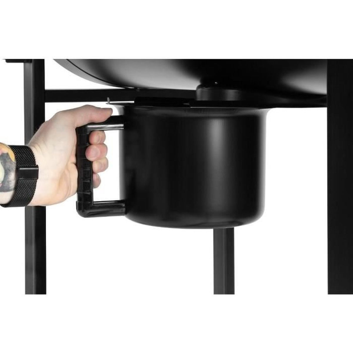 A hand holding a black handle attached to a black container. The container is part of a grill. The background is blurred.