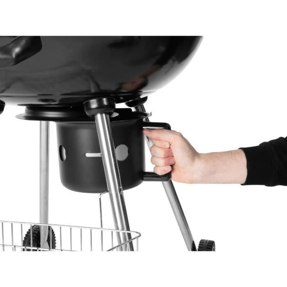 A hand holds the black handle of a charcoal grill. The grill is black and silver, with a round bowl and legs. White background.