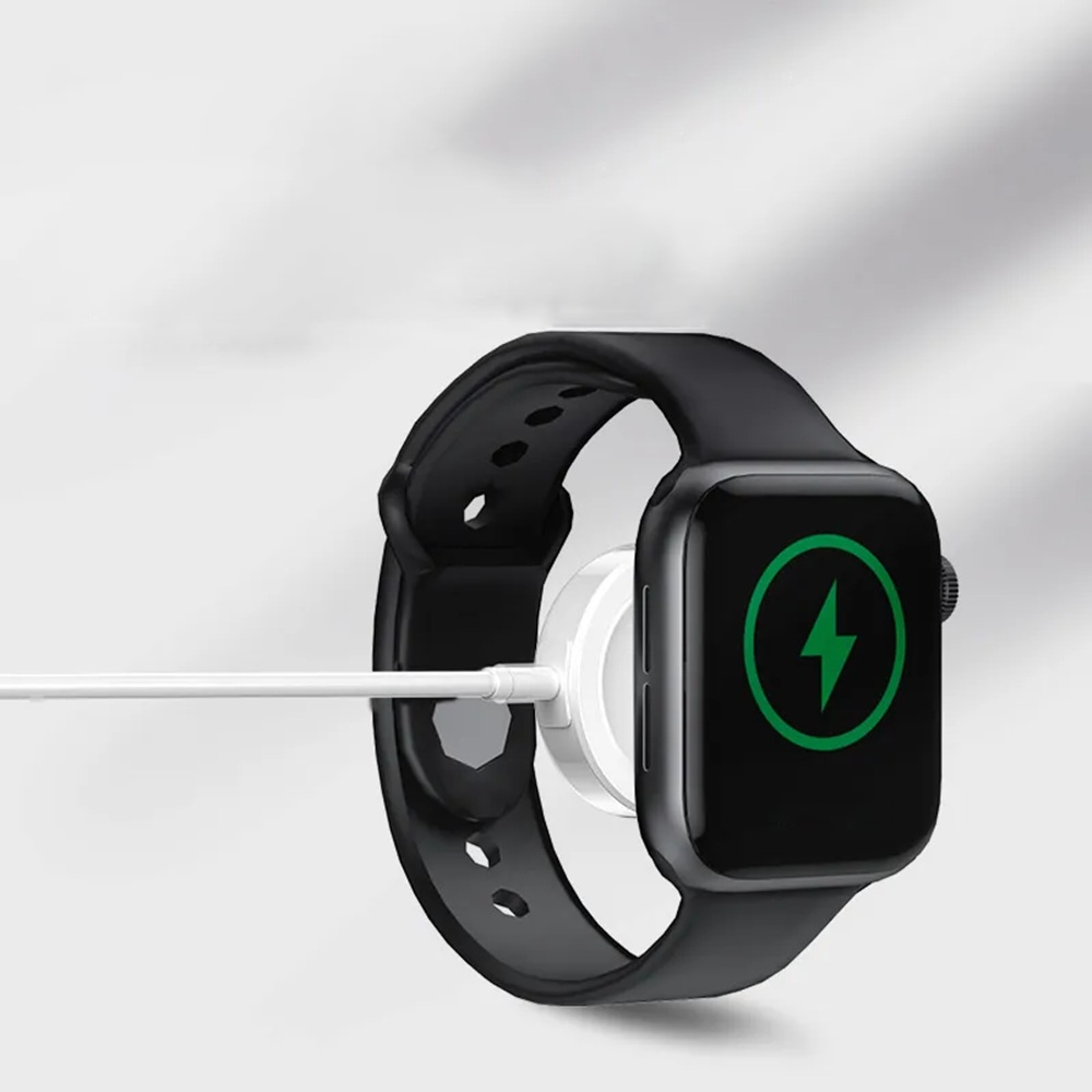 Schwarze Apple Watch wird geladen. Bildschirm zeigt grünen Blitz. Weißes Ladekabel angeschlossen. Schwarzes Armband. Weißer Hintergrund.