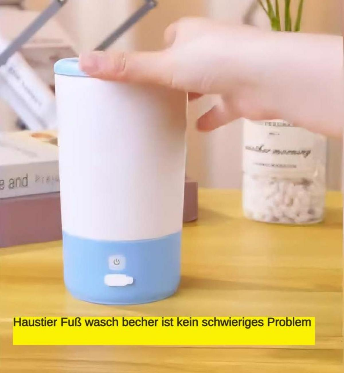 Eine Hand berührt ein weiß-blaues Gerät mit einem Knopf auf einem Holztisch. Ein Buch und ein Glas mit Pflanzen sind im Hintergrund.