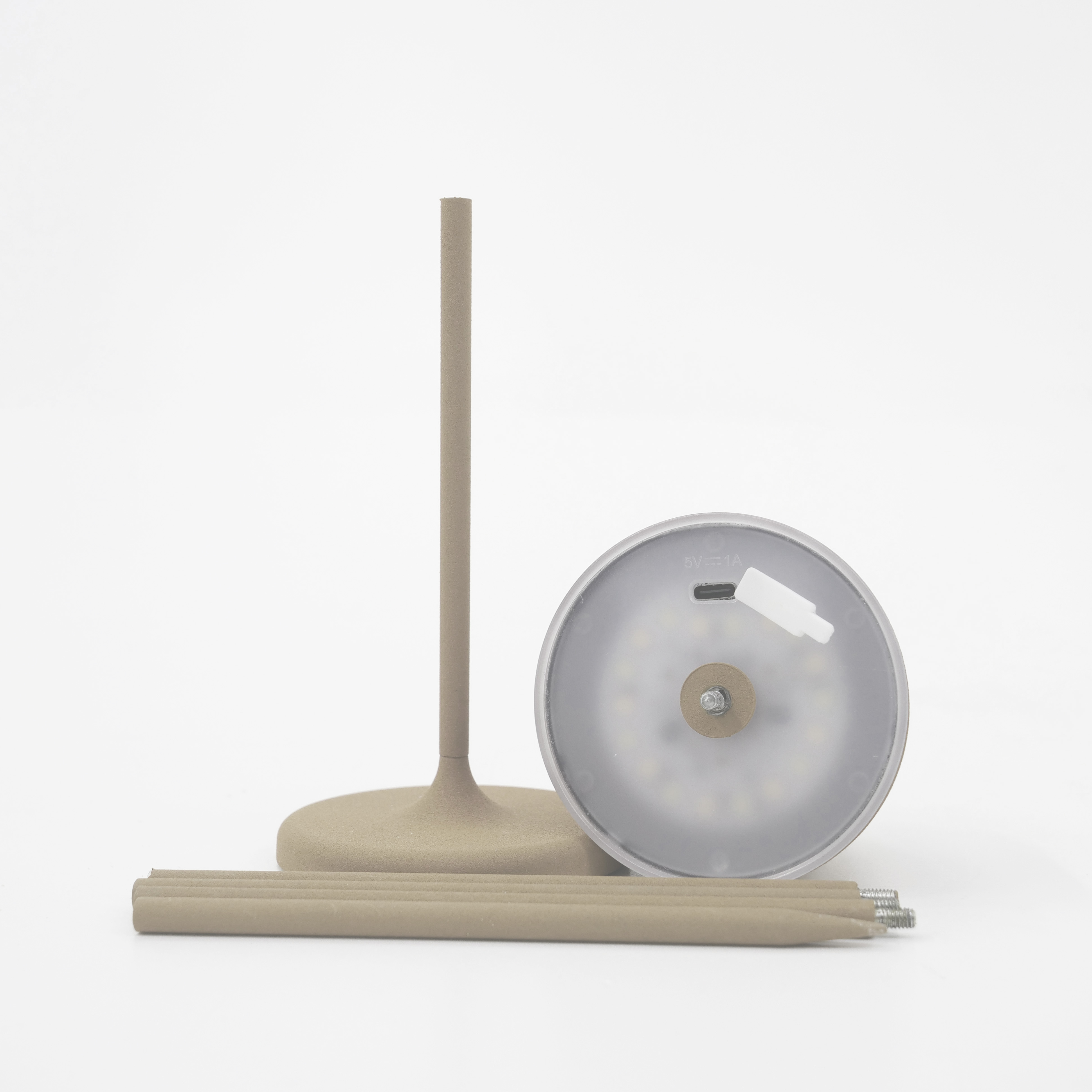 Eine zerlegte Lampe liegt auf einer weißen Oberfläche. Teile umfassen Licht, Ständer und zwei Stäbe.