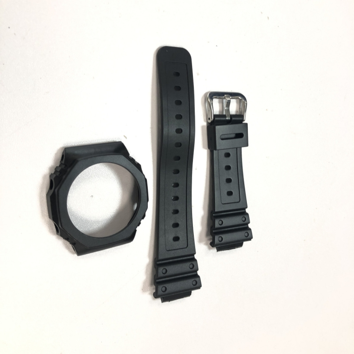 Schwarze Uhrenkomponenten auf weißer Oberfläche: eine Lünette, Uhrenarmbandteile.