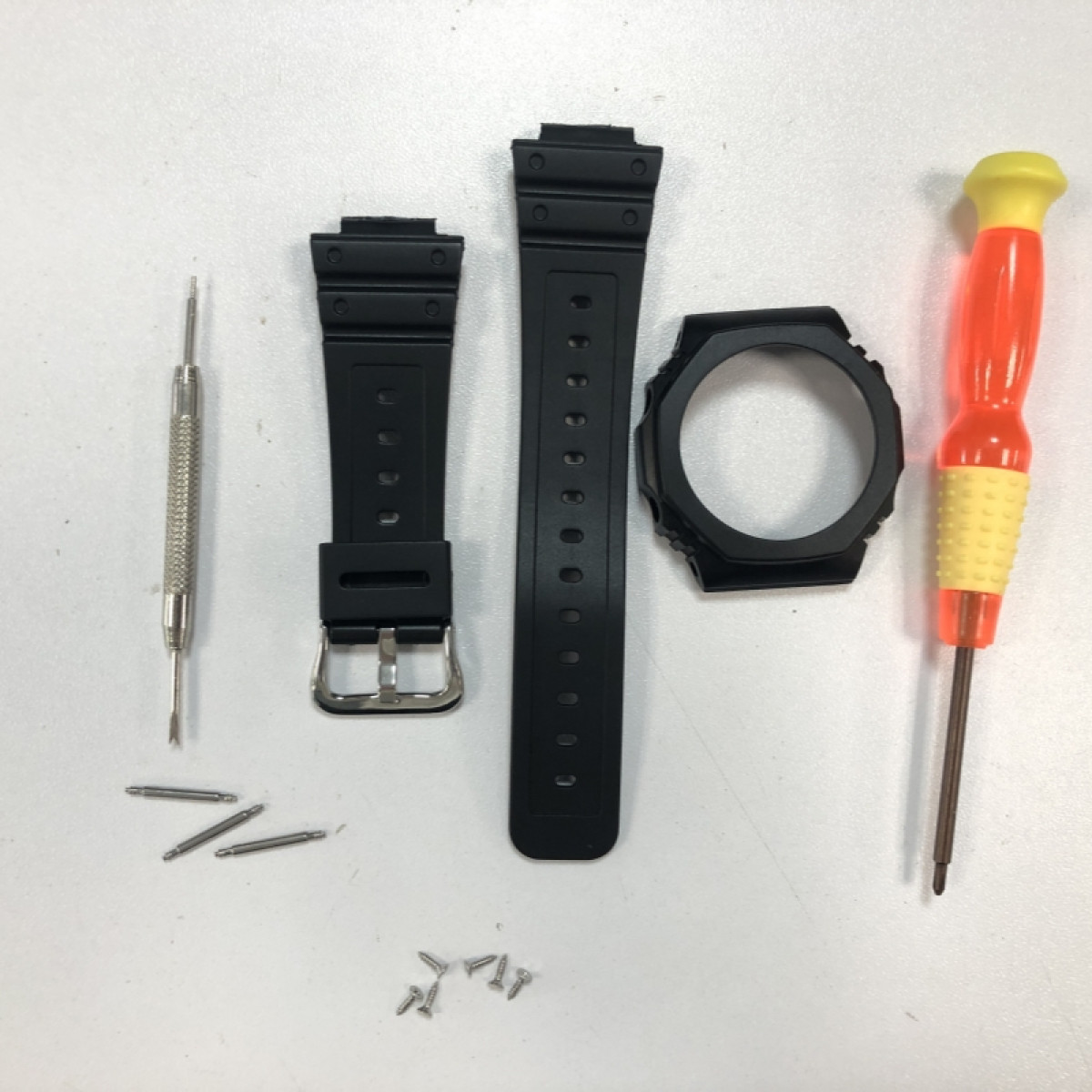 Uhrreparaturteile: Uhrenarmbänder, Lünette, Schraubendreher, Stifte und Schrauben auf weißer Oberfläche.