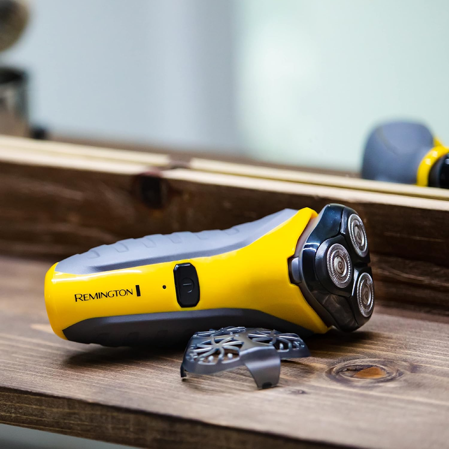 Un rasoio elettrico Remington giallo e grigio su una superficie di legno. La testina del rasoio è visibile, con una lamina staccata.