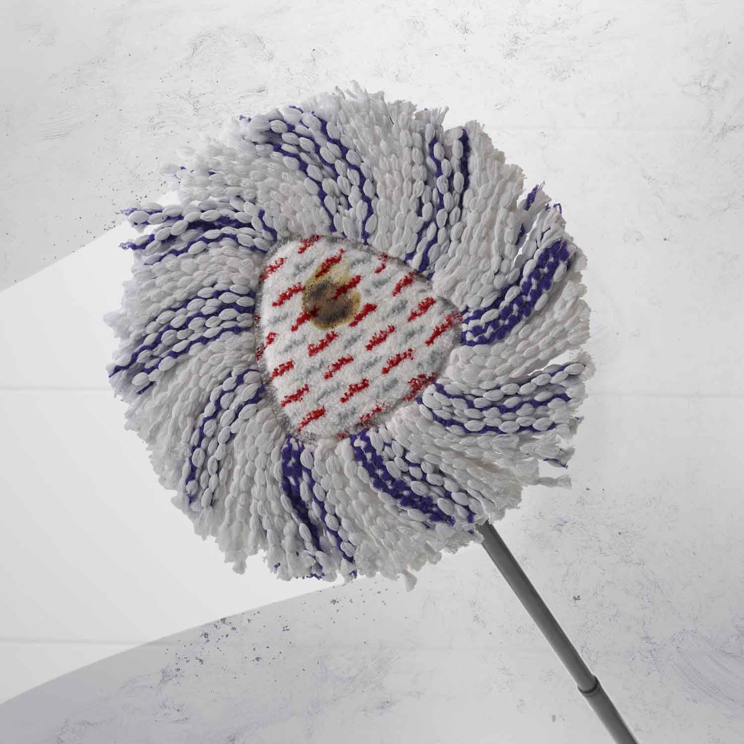 Primer plano de un cabezal de fregona. El cabezal de la fregona es blanco, morado y rojo. El fondo es blanco con algunas marcas.