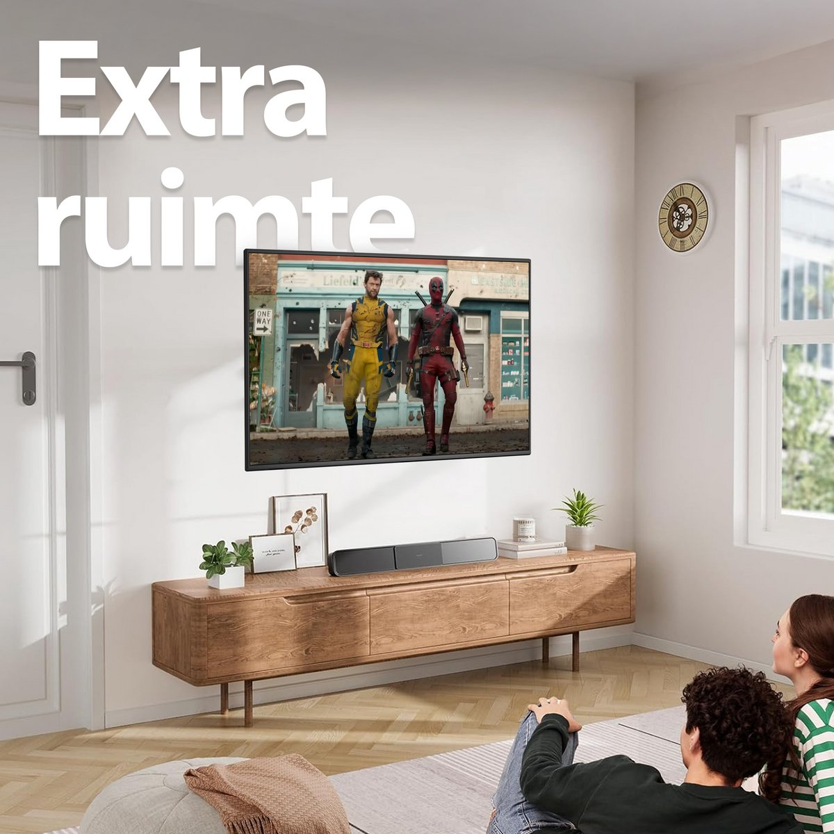 A living room with a TV showing Wolverine and Deadpool. A wooden cabinet holds a soundbar, and a couple watches.