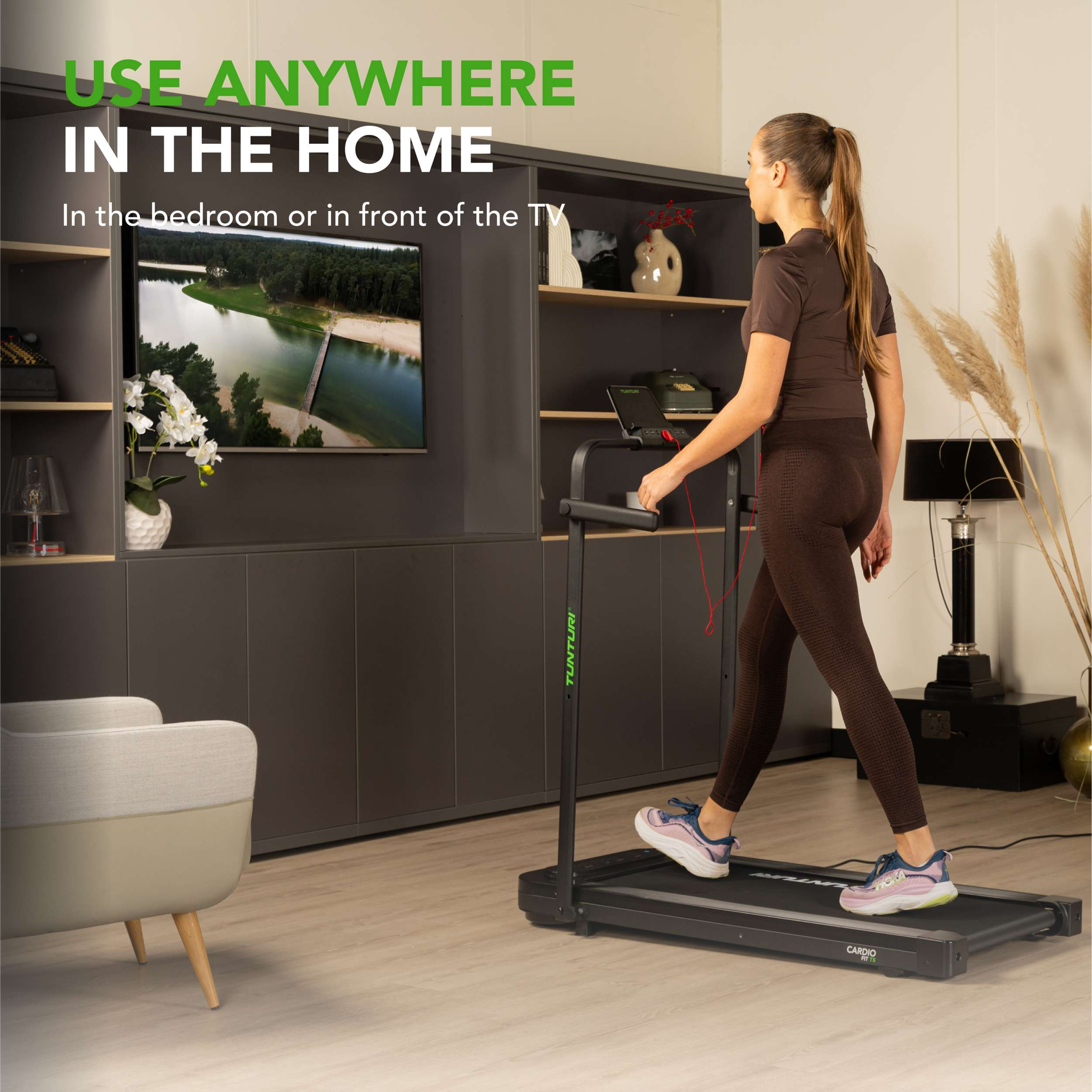 Een vrouw traint op een loopband. De scène is in een kamer met een tv en een kast.