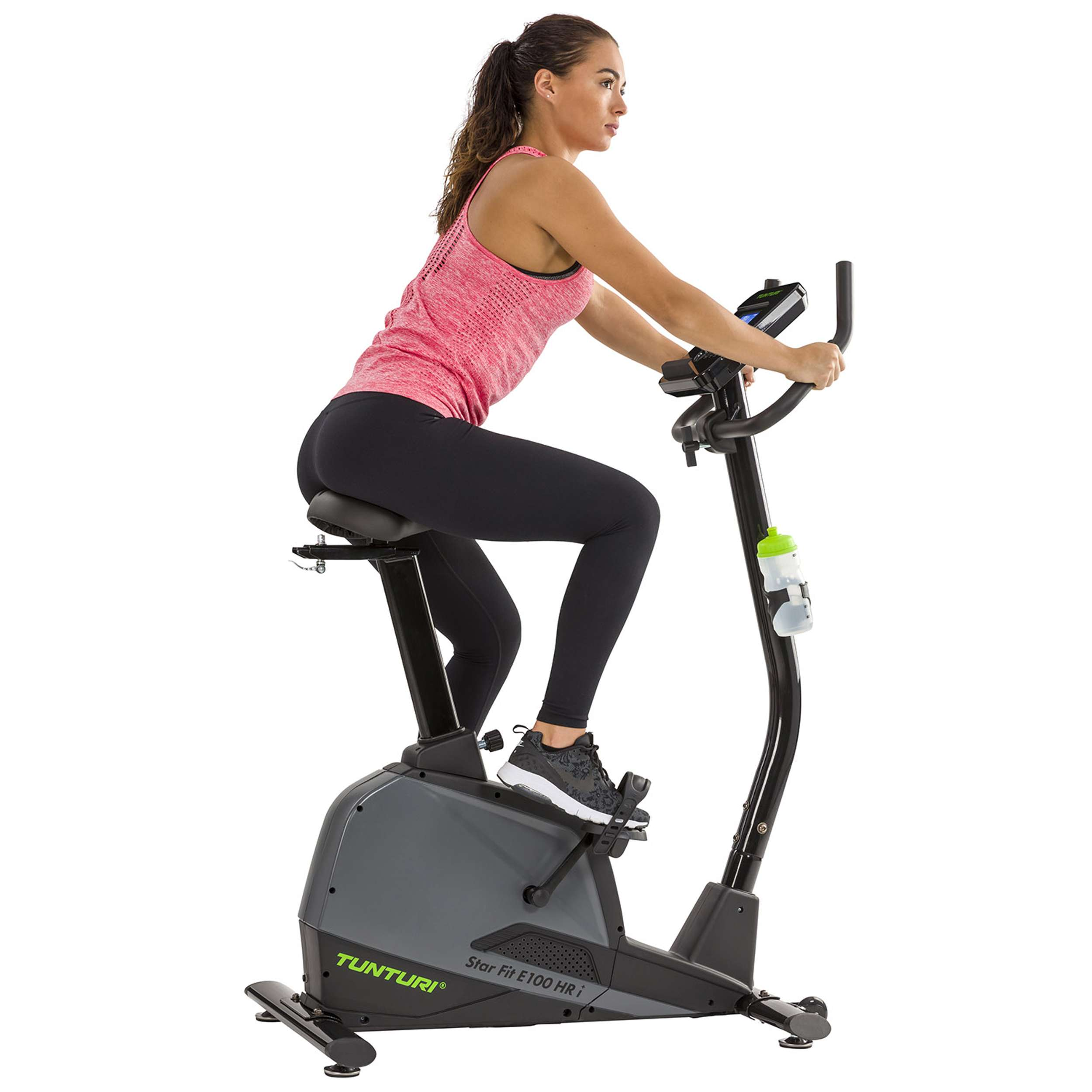 Vrouw op hometrainer. Draagt roze top en zwarte legging. De fiets is grijs en zwart.