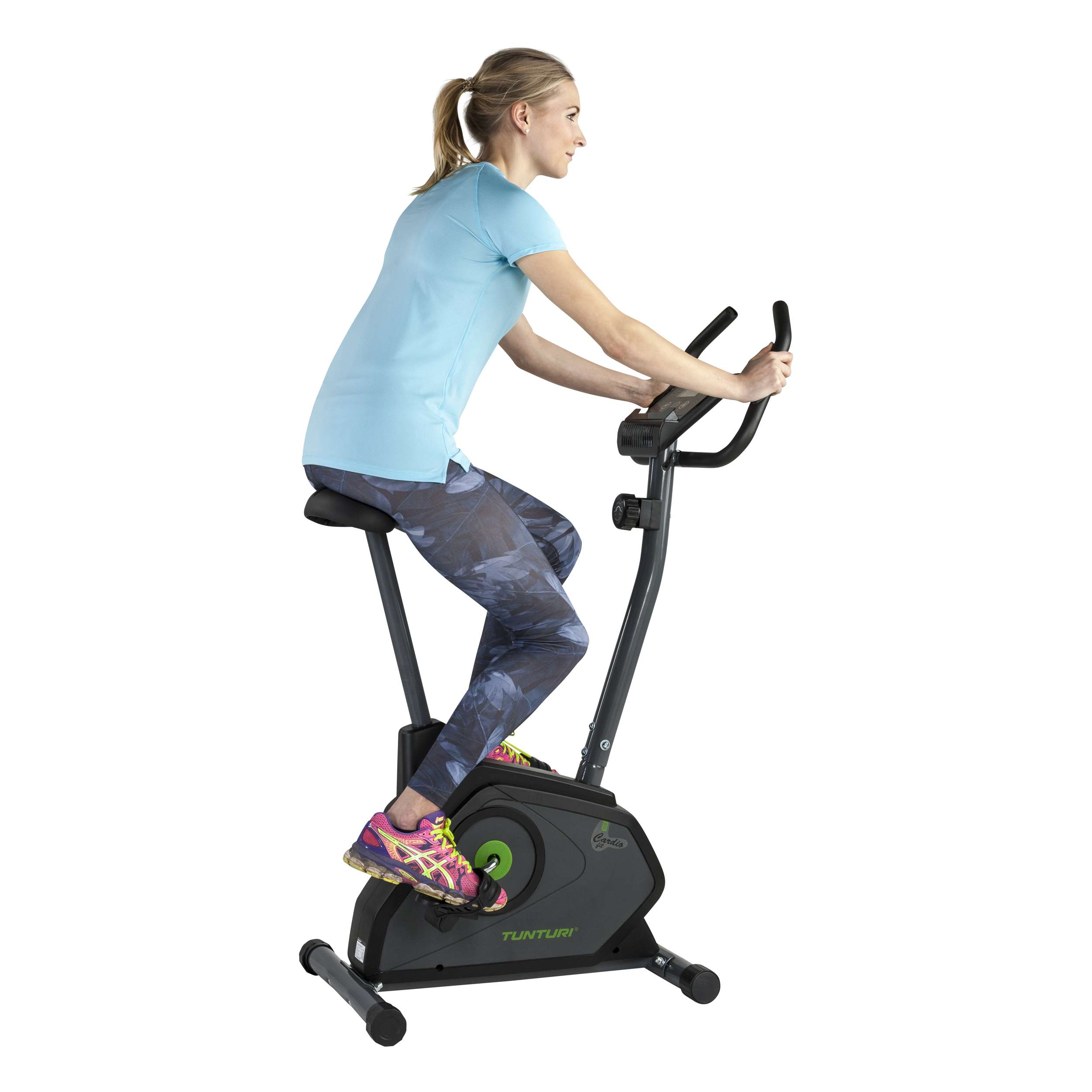 Een vrouw in een blauwe top en een legging met patroon fietst op een Tunturi hometrainer. De achtergrond is wit.