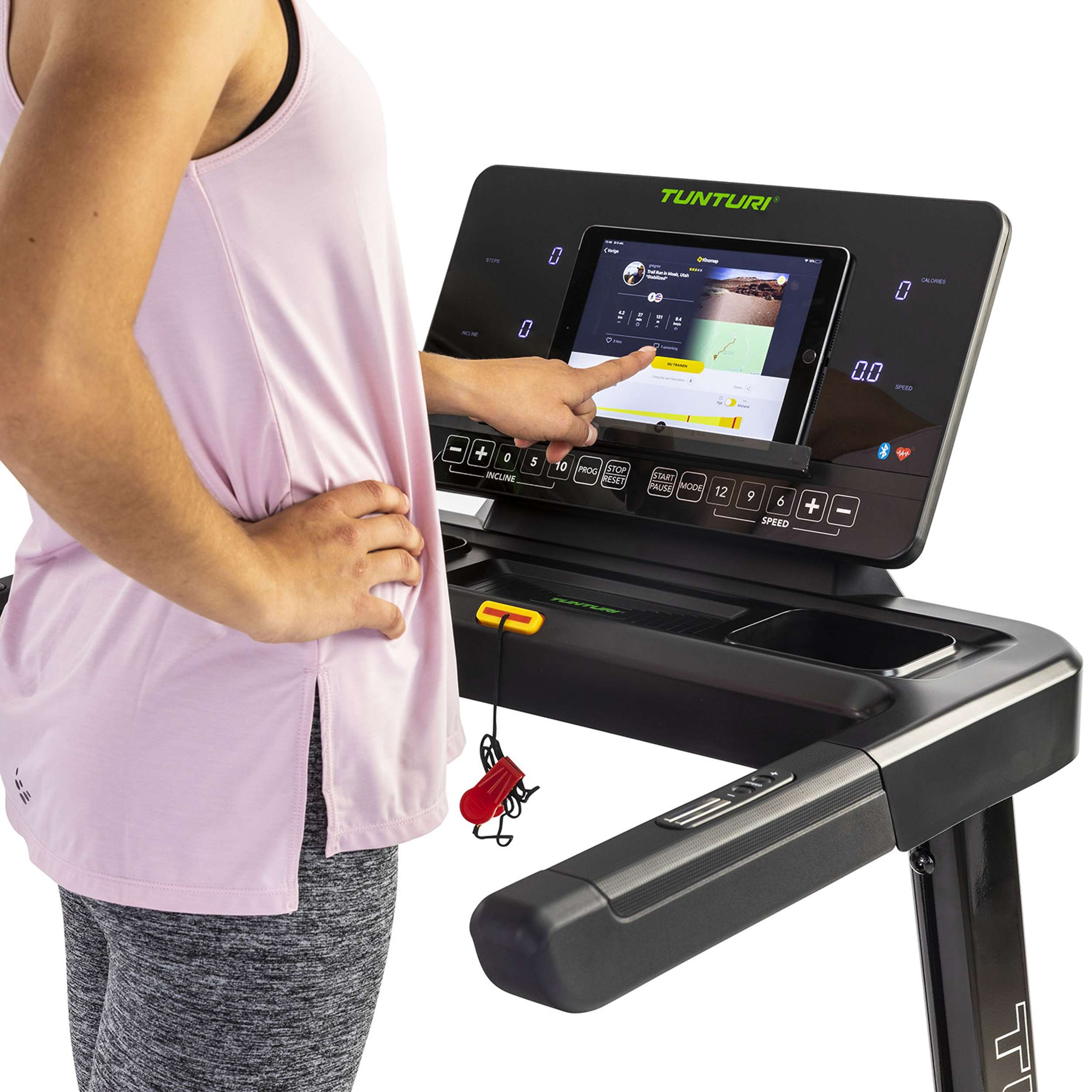 Een persoon die een Tunturi loopband gebruikt. De persoon wijst naar het scherm, dat trainingsgegevens laat zien. Roze top, grijze legging.