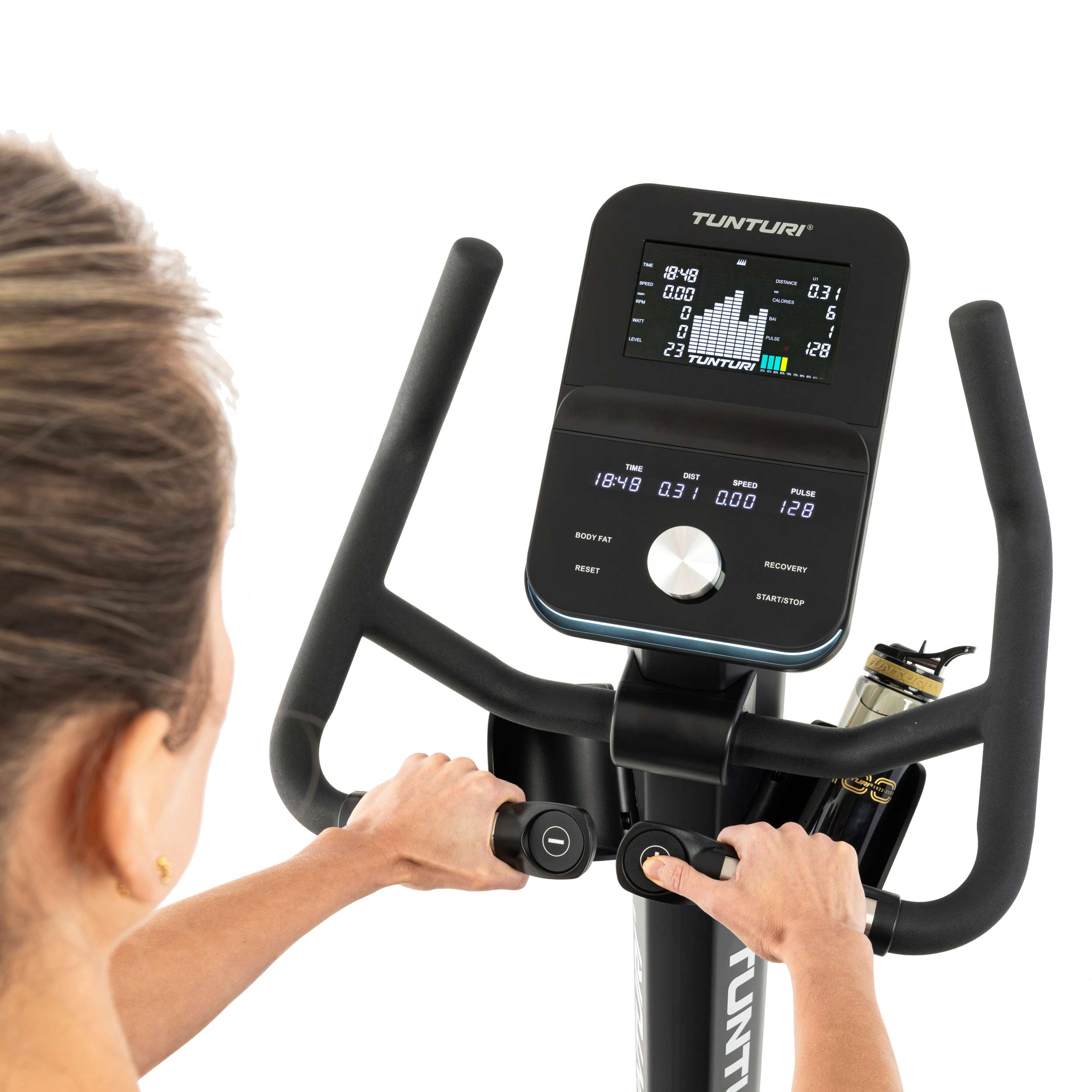 Persoon op een hometrainer. Het display toont tijd, afstand, snelheid en hartslag. Er is een waterfles aanwezig.