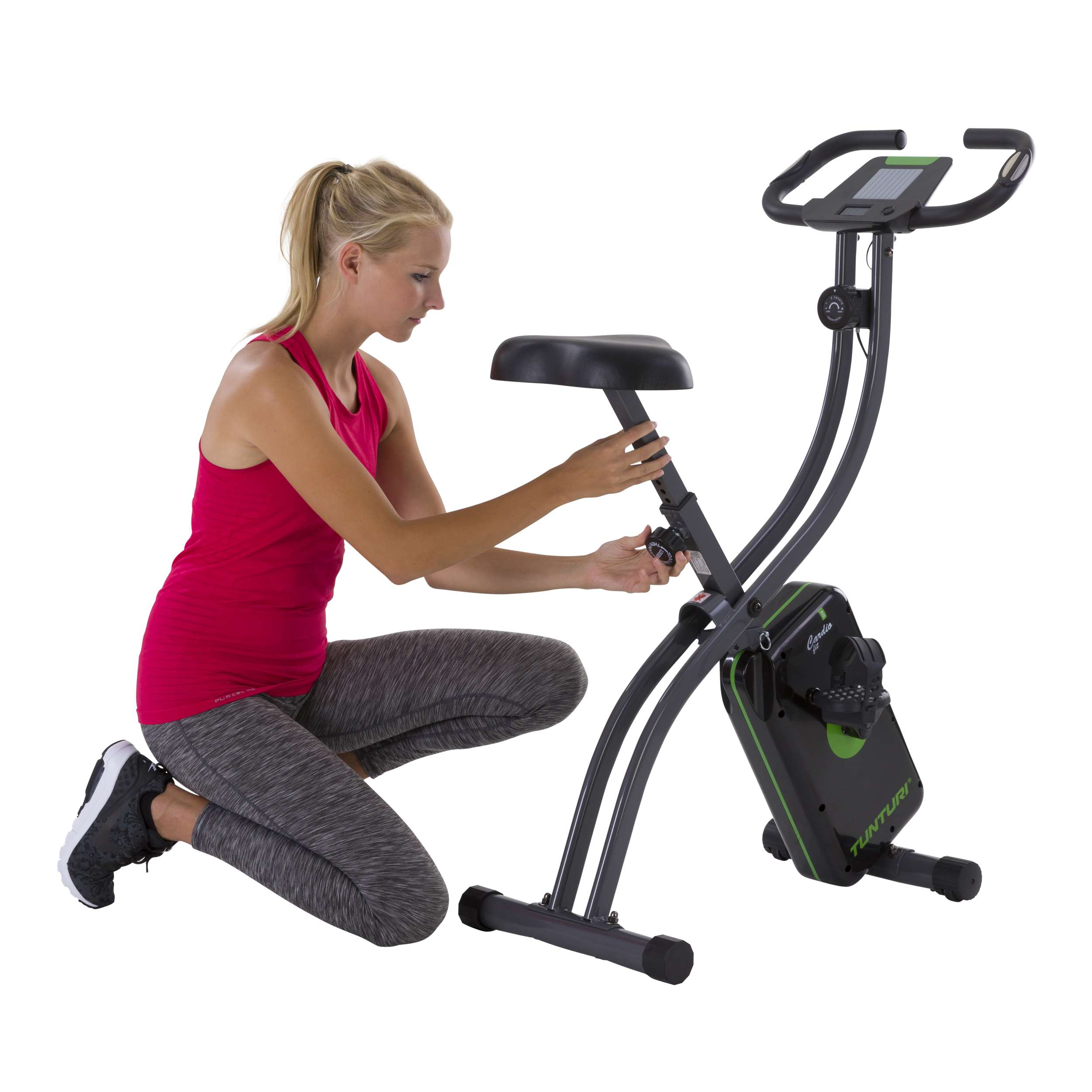 Een vrouw verstelt de zitting van een hometrainer. Ze draagt een rode tanktop en grijze leggings.