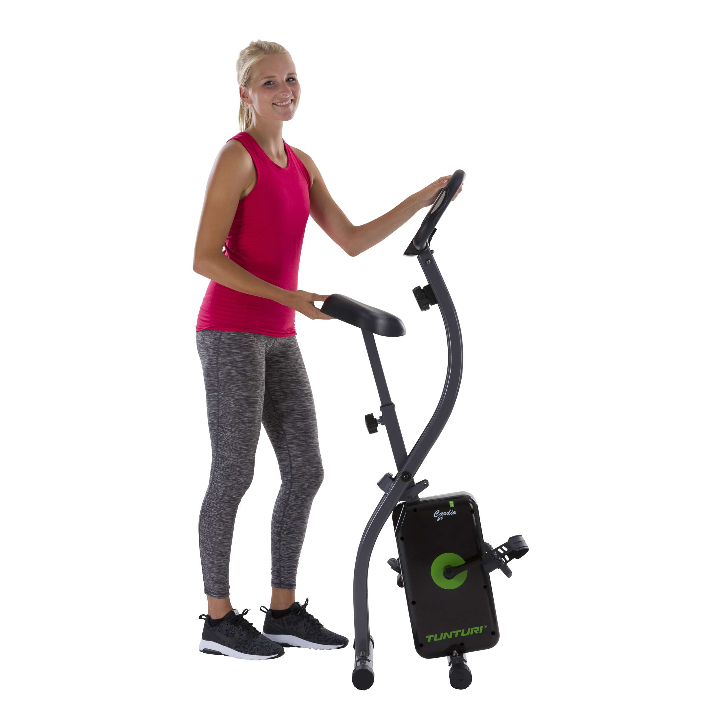Vrouw in sportkleding met een hometrainer. Ze glimlacht. De fiets is zwart en groen.