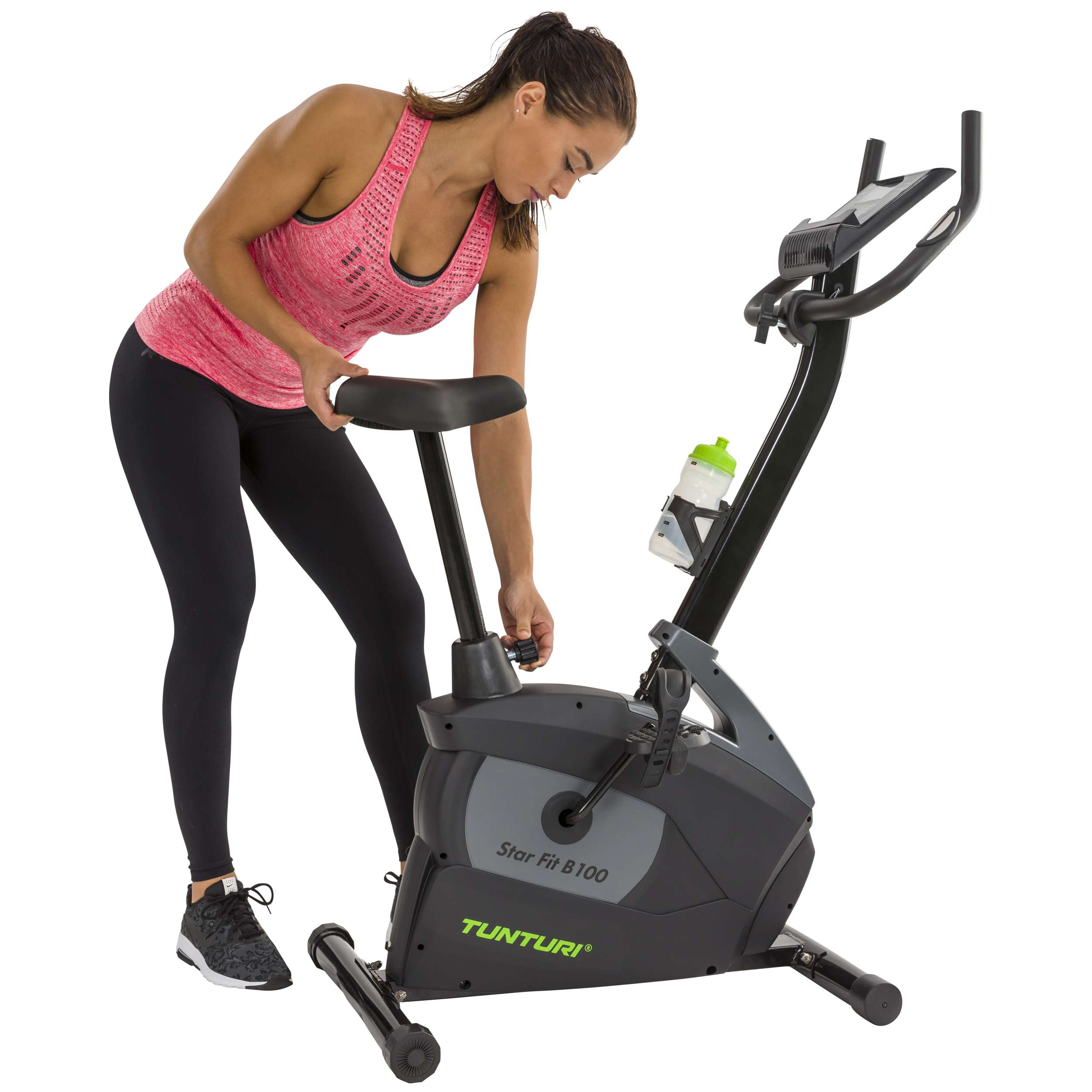 Een vrouw stelt een hometrainer af. Ze draagt een roze top en zwarte legging. De fiets is zwart en grijs.