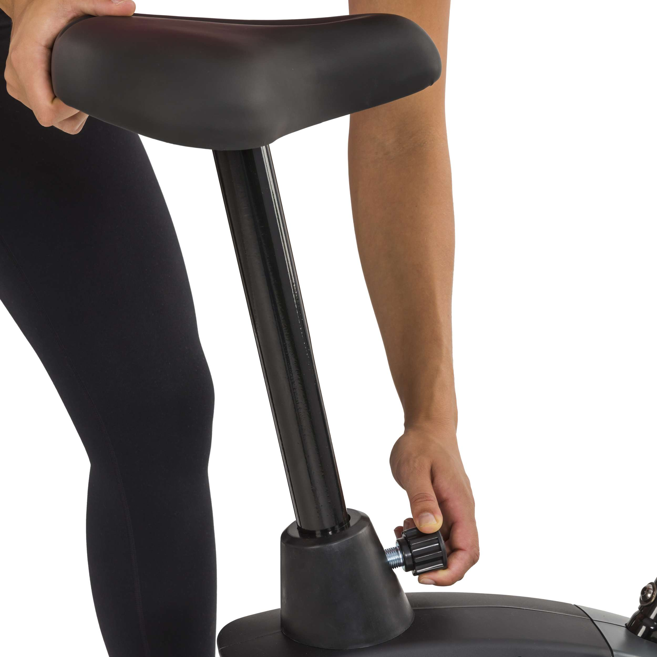 Een persoon past de zitting van een hometrainer aan. De zitting en de fiets zijn zwart. De persoon draagt een zwarte legging.