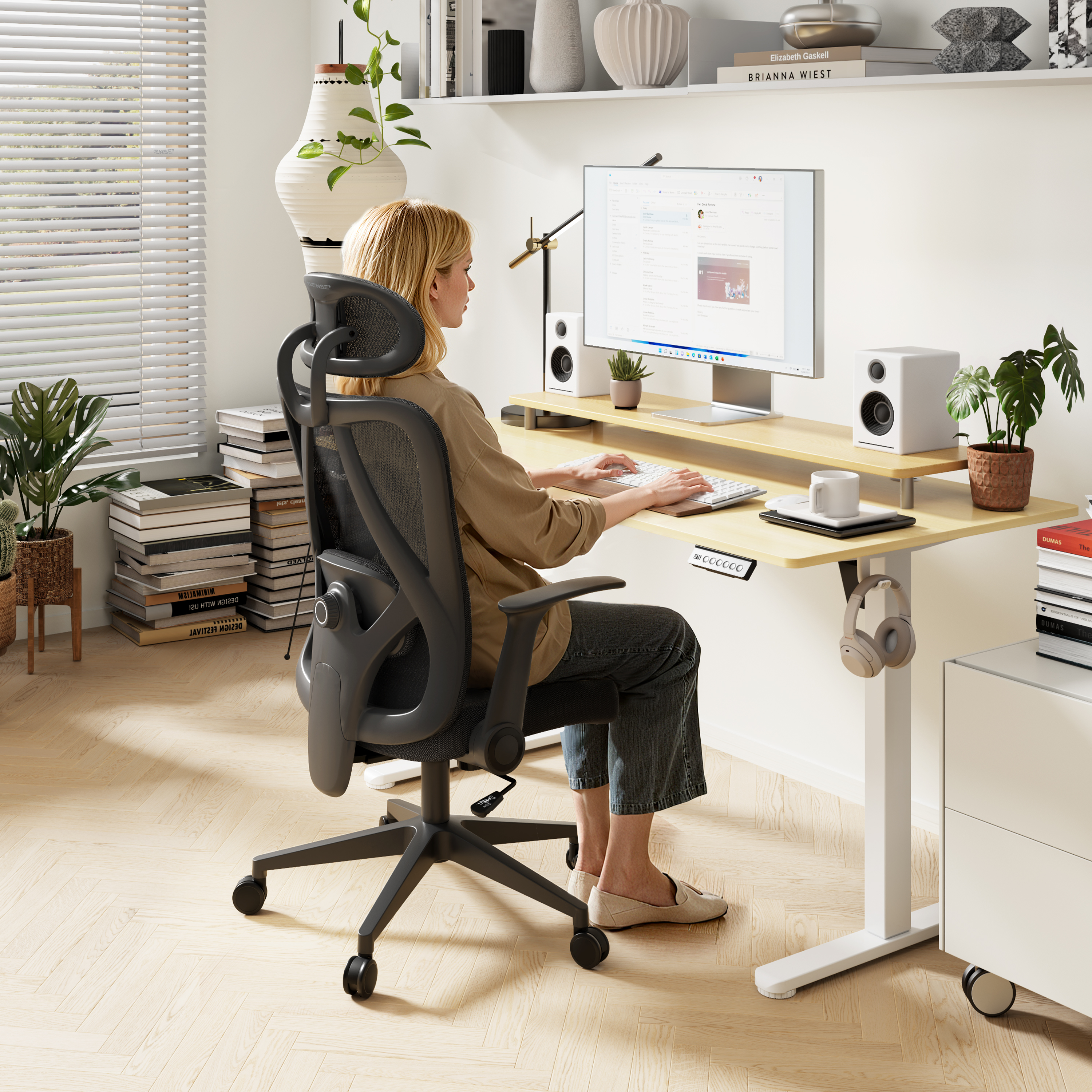 Una donna è seduta a una scrivania, che digita su una tastiera. Un monitor, altoparlanti e piante sono sulla scrivania.