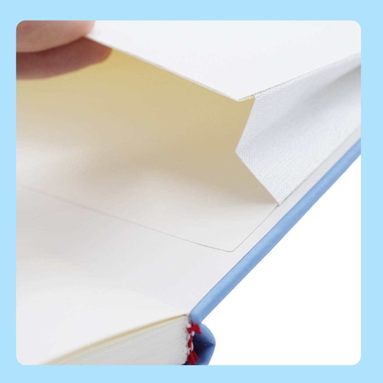 Nahaufnahme eines Buches mit weißen Seiten, blauem Buchrücken und einer Hand, die einen Umschlag anhebt. Die Innenseite ist beige.