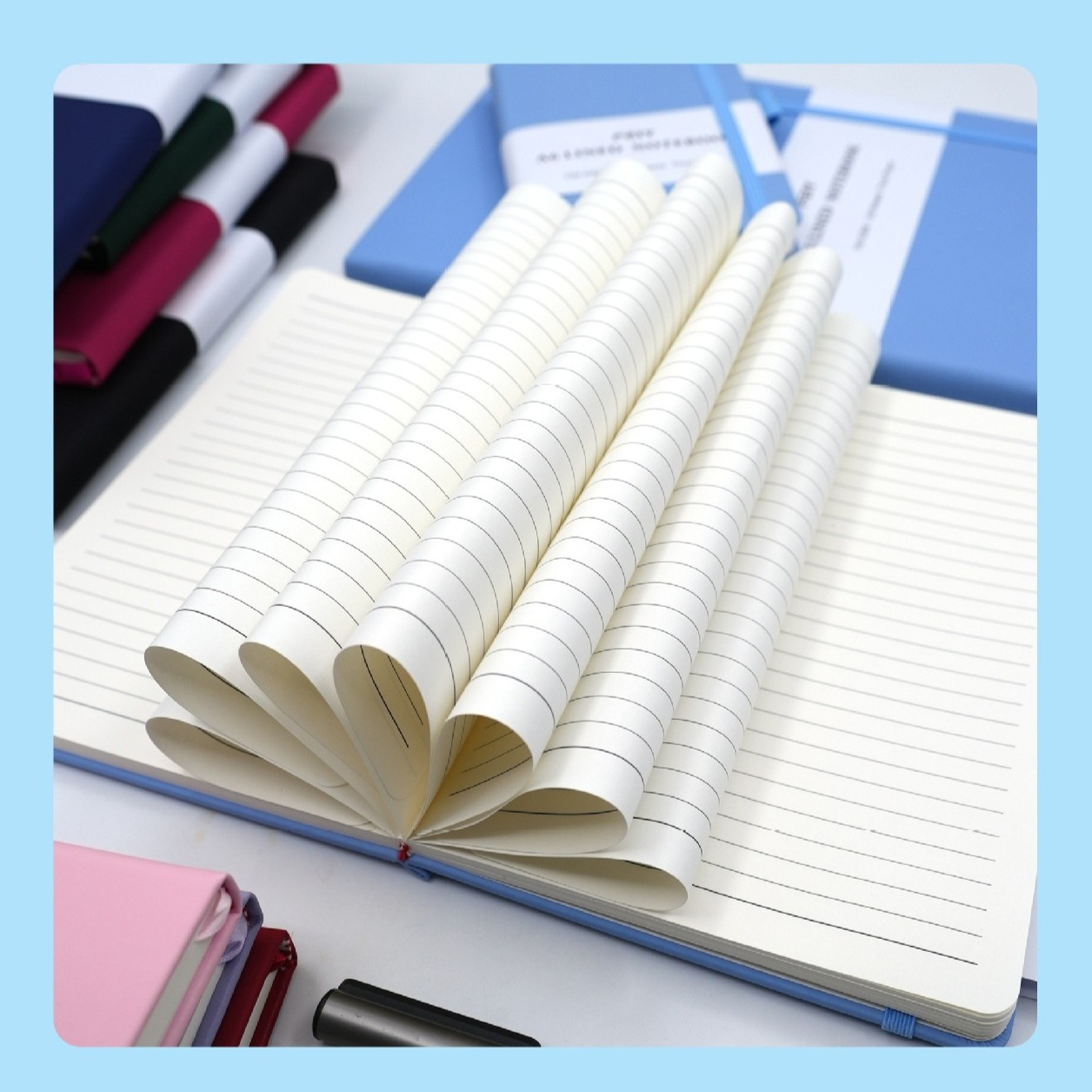 Ein offenes liniertes Notizbuch mit aufgefächerten Seiten. Andere Notizbücher in Blau, Rosa und Schwarz sind im Hintergrund, zusammen mit einem Stift.