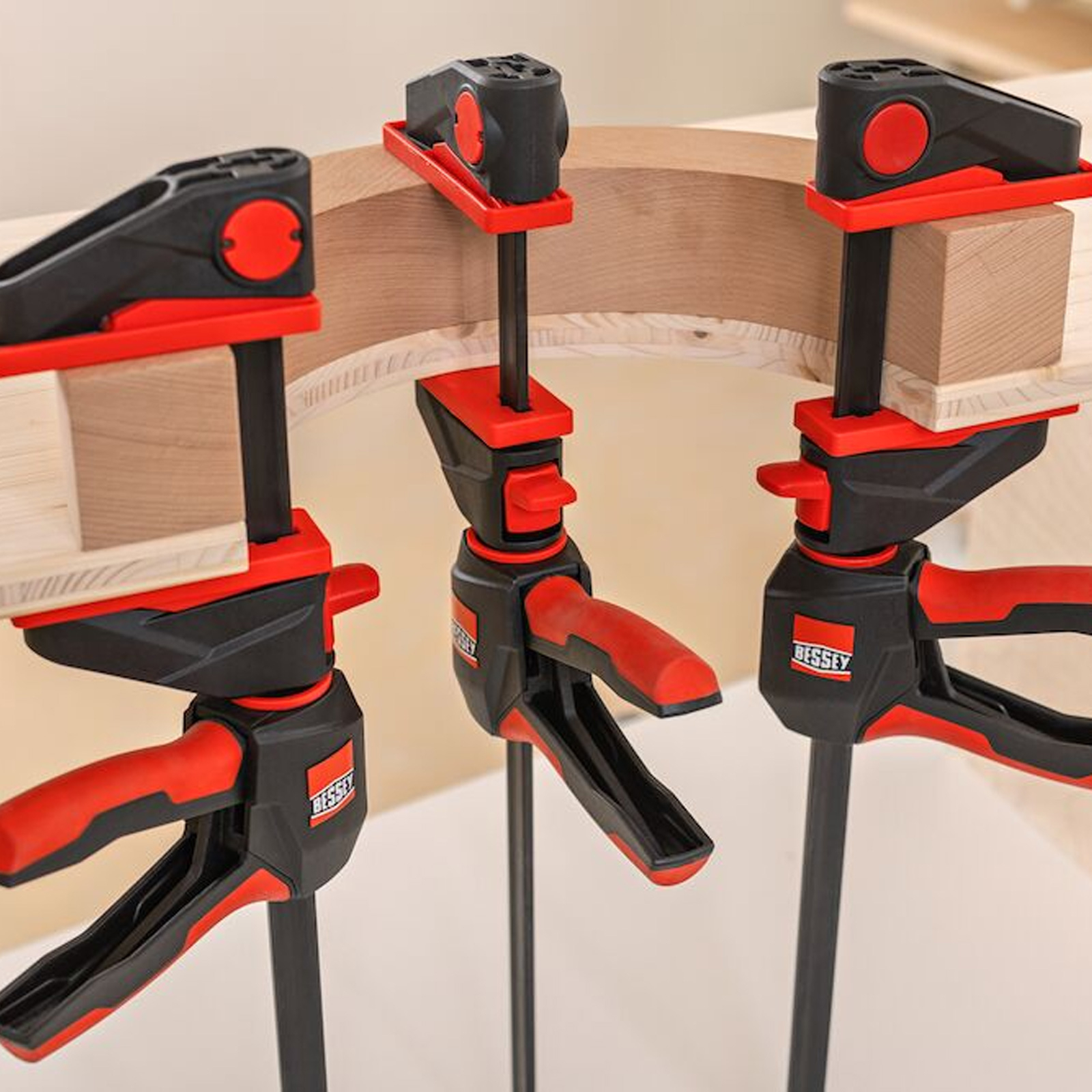Drei Klemmen sichern ein gebogenes Holzstück. Klemmen sind schwarz und rot und halten Blöcke am Holz fest.
