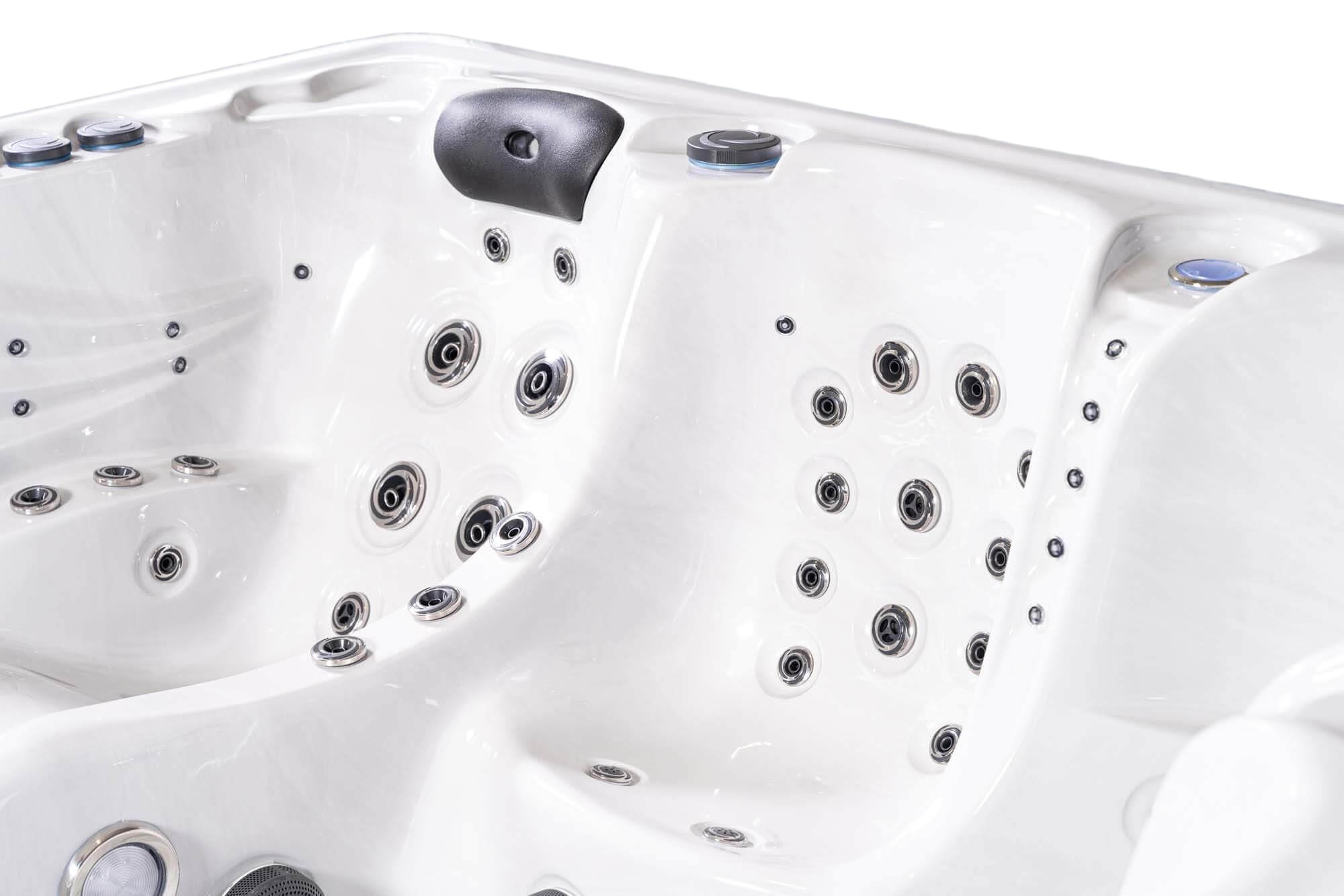 Nahaufnahme des Inneren eines weißen Whirlpools. Es verfügt über zahlreiche Düsen, Bedienknöpfe und eine Kopfstütze. Die Düsen sind silbern, und die Wanne ist sauber.