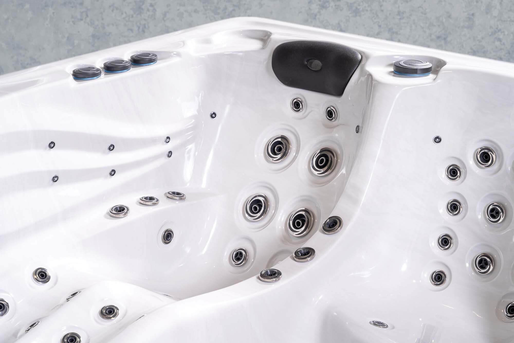 Ein weißes Whirlpool-Interieur mit verschiedenen Düsen und Bedienelementen. Mit schwarzer Kopfstütze und Wasserdüsen.