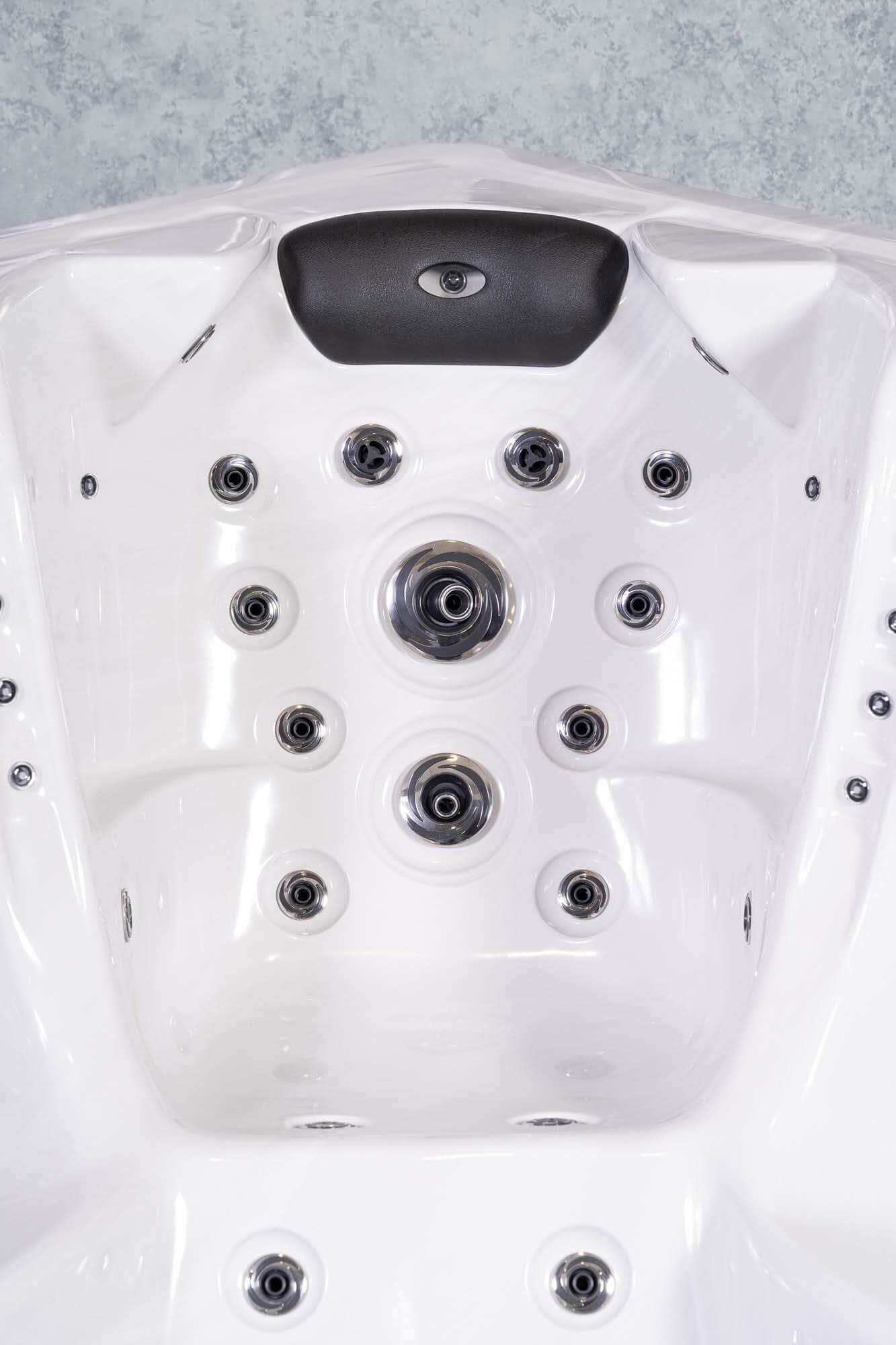 Innenraum eines weißen Whirlpools mit mehreren Wasserdüsen. Oben befindet sich eine schwarze Kopfstütze. Der Hintergrund ist eine hellgraue Wand.