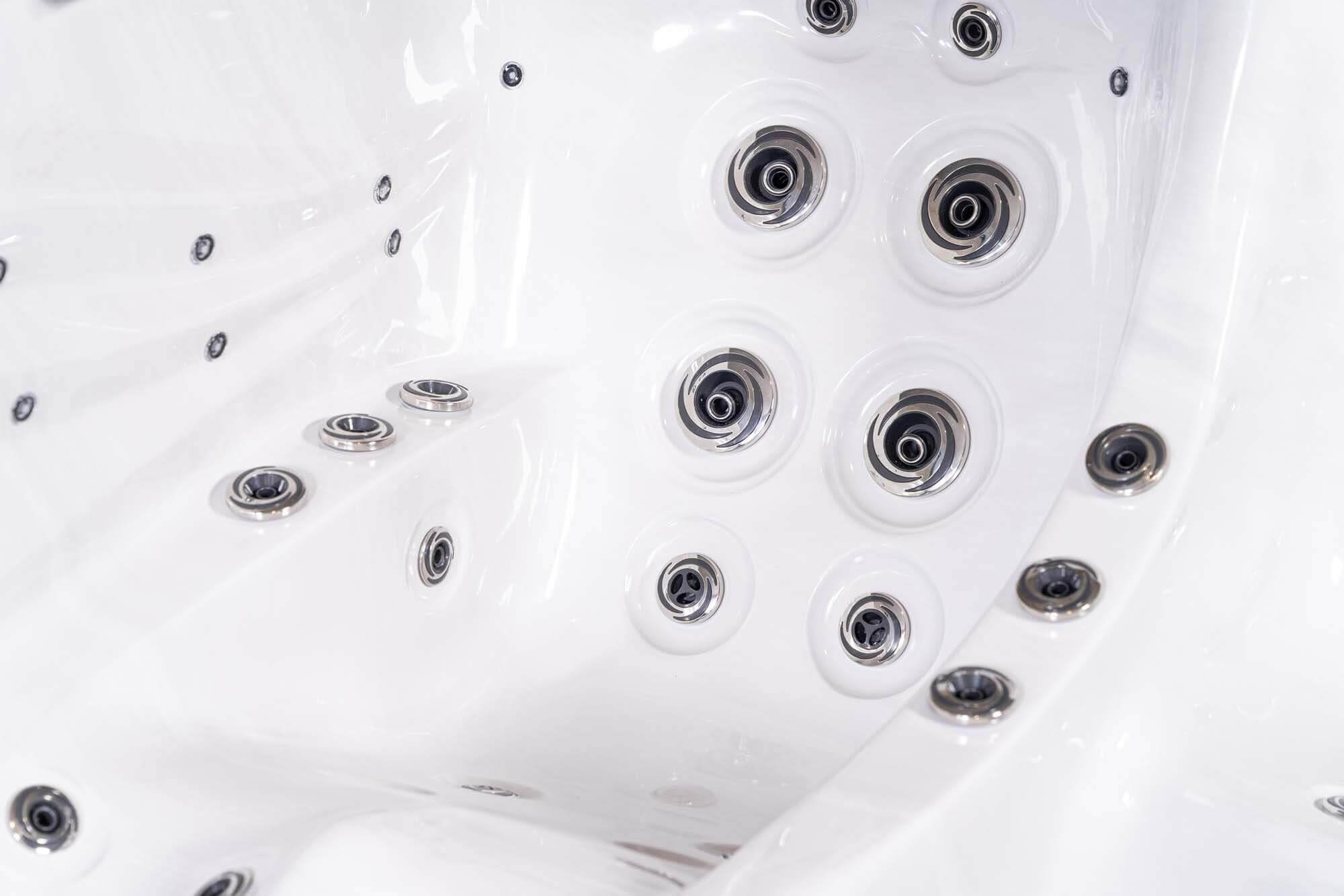 Nahaufnahme eines weißen Whirlpool-Innenraums mit mehreren Düsen. Die Düsen haben silberne Verzierungen und sind kreisförmig angeordnet.