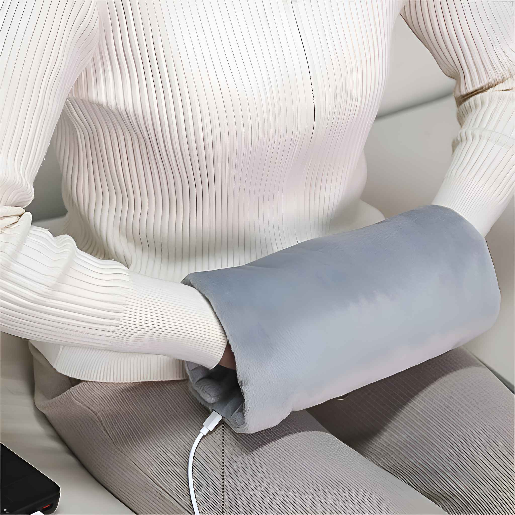 Eine Person mit weißem Pullover benutzt einen grauen Handwärmer. Ein USB-Kabel ist an den Wärmer angeschlossen.