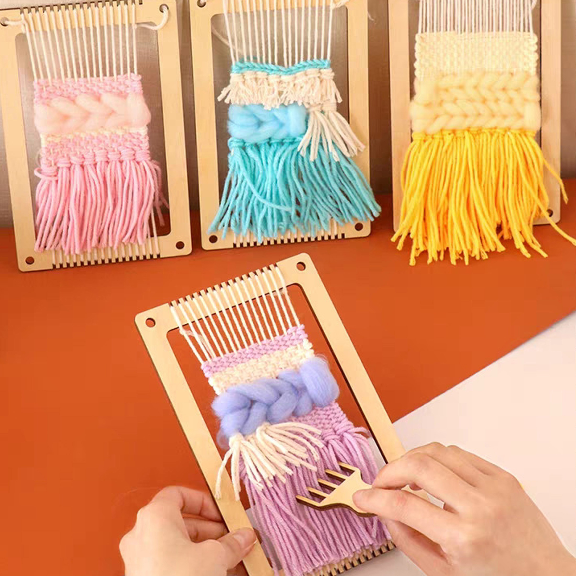 Webstühle mit bunten Garnen in Pink, Blau und Gelb. Eine Person benutzt einen Kamm auf dem Webstuhl.