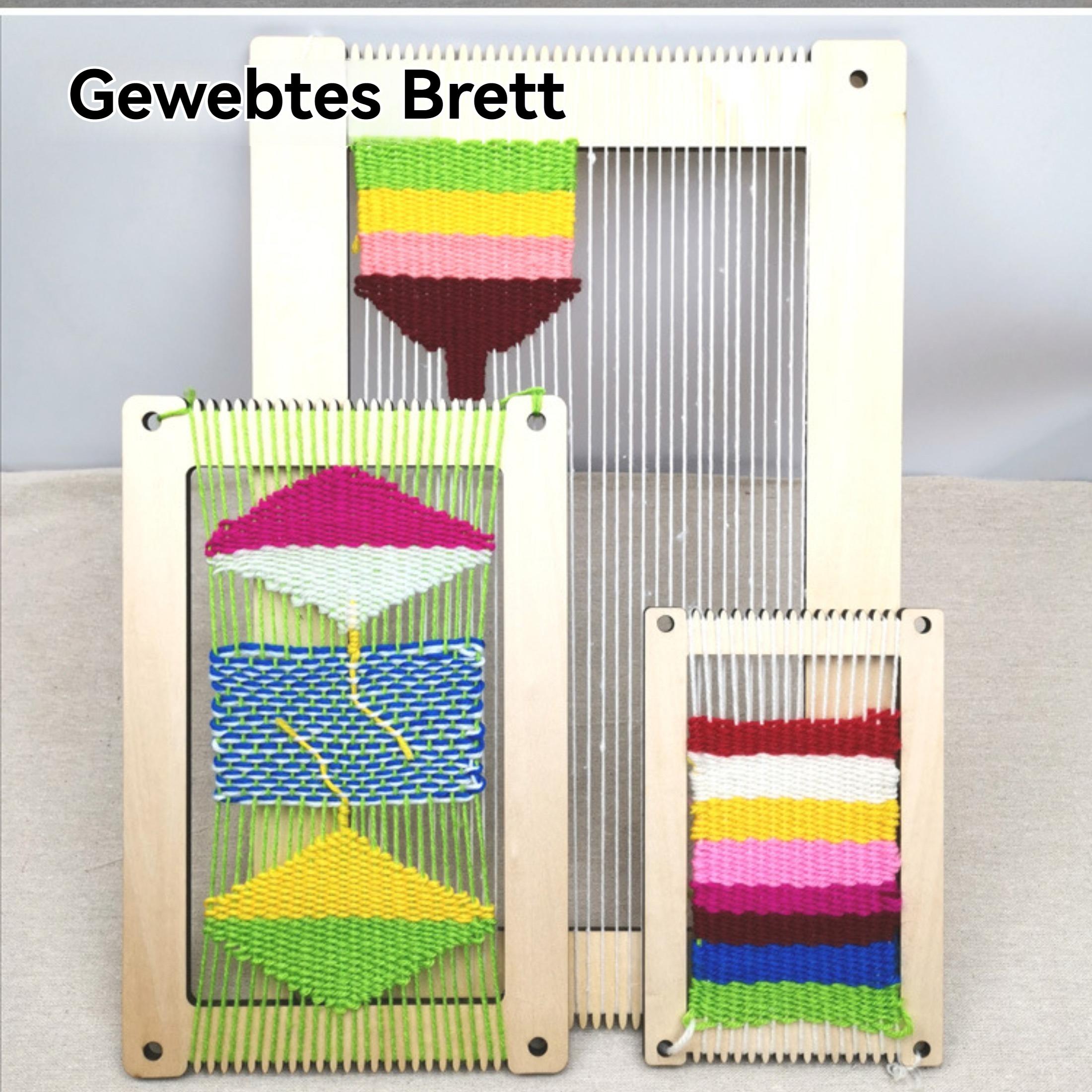 Drei hölzerne Webrahmen mit bunten Webmustern. Grüne, rosa, gelbe und blaue Fäden sind sichtbar. Der Hintergrund ist heller Stoff.