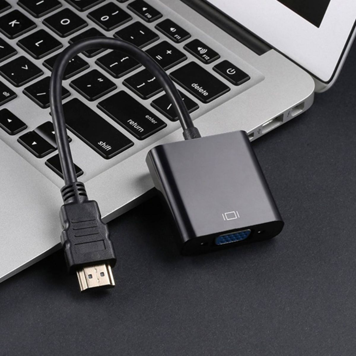 Ein HDMI-zu-VGA-Adapter liegt neben einem Laptop. Der Adapter ist schwarz und mit einem schwarzen Kabel verbunden.