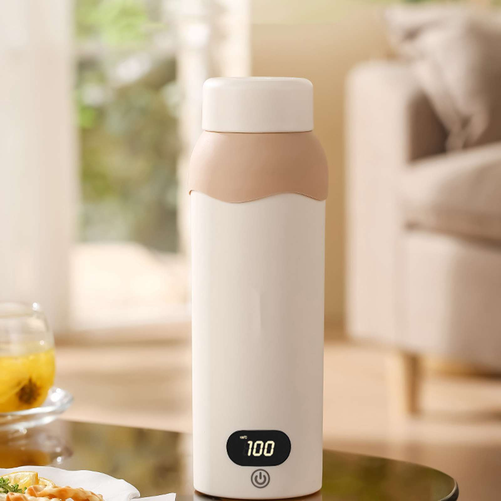 Weiße und beige isolierte Wasserflasche mit Temperaturanzeige, die 100 Grad anzeigt. Im Hintergrund befinden sich eine Couch und ein Tisch.