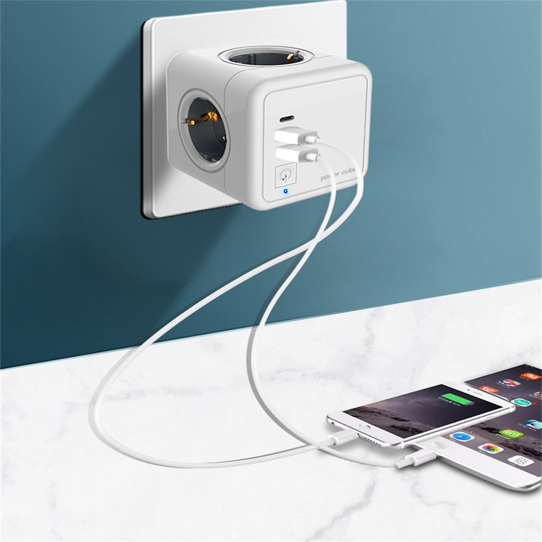 Weißer Power Cube mit Steckdosen und USB-Anschlüssen, verbunden mit zwei ladenden Telefonen. Blauer Wandhintergrund und weißer Tisch.