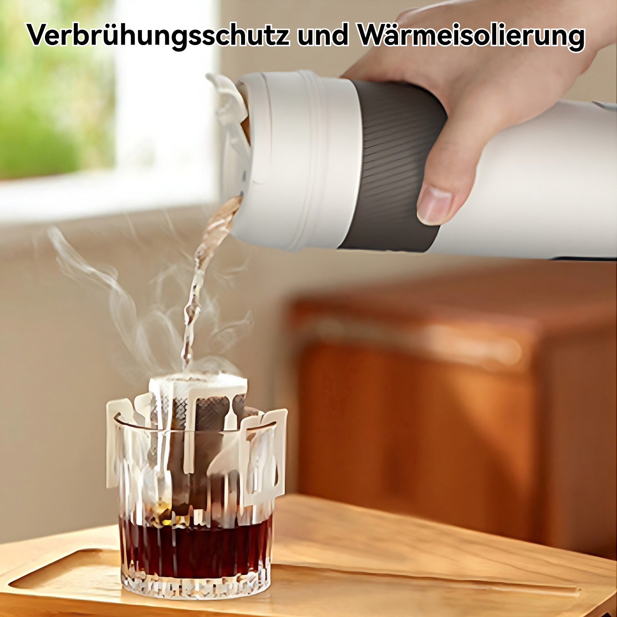 Eine Hand gießt heißes Wasser aus einer weißen Thermoskanne in ein Glas mit Kaffeefilter. Dampf steigt auf. Holztisch.