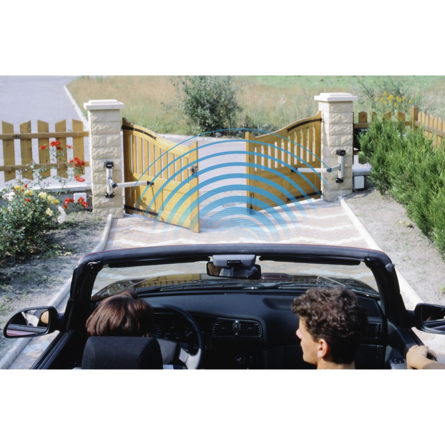 Ein Cabrio nähert sich einem automatischen Tor. Zwei Personen sind darin. Blaue wellenartige Signale gehen vom Tor aus.