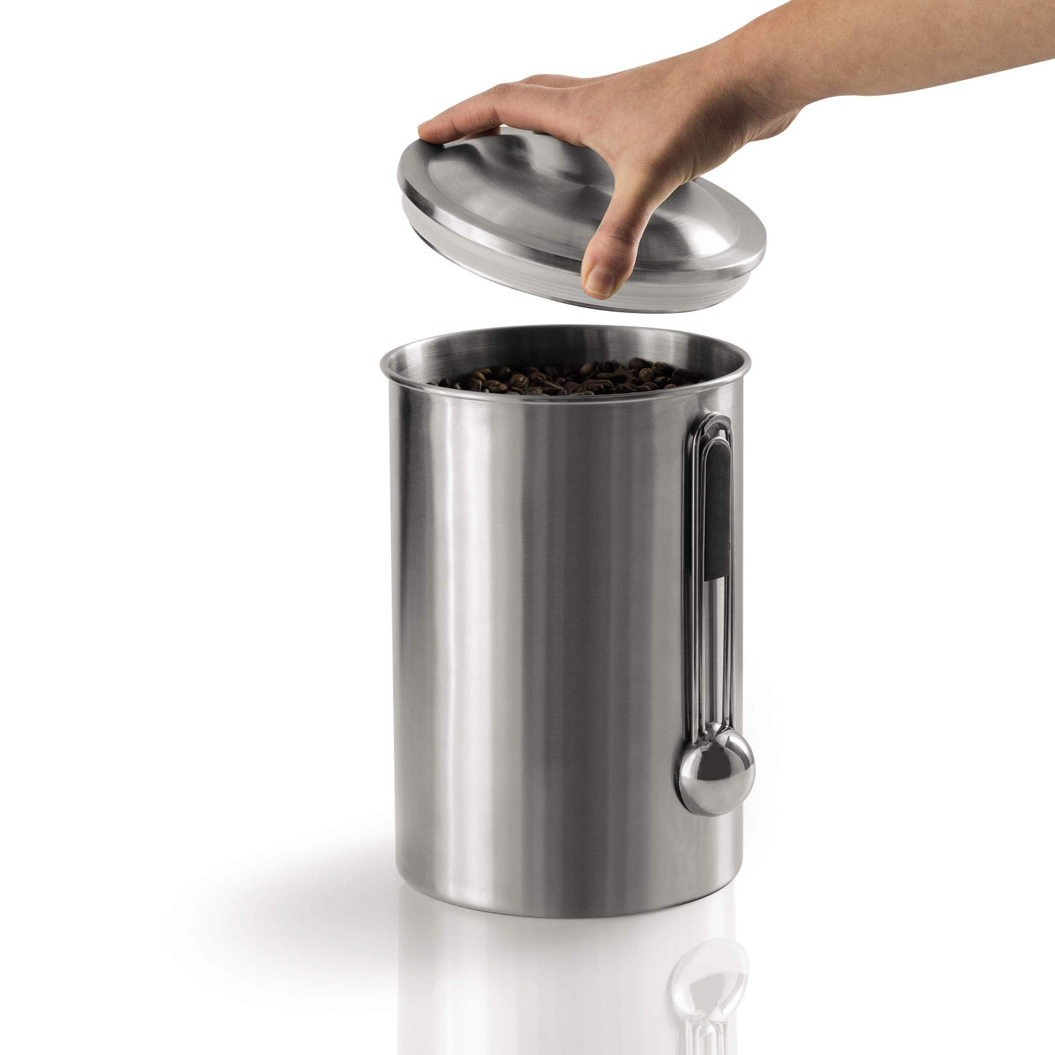 Eine Hand hebt den Deckel von einem silbernen Kaffeebehälter, der mit Kaffeebohnen gefüllt ist. Ein Messlöffel ist befestigt.