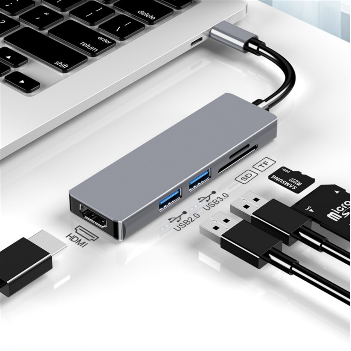 Ein silberner USB-Hub ist mit einem Laptop verbunden. Er hat HDMI-, USB- und SD-Karten-Steckplätze. Kabel und Speicherkarten sind ebenfalls sichtbar.