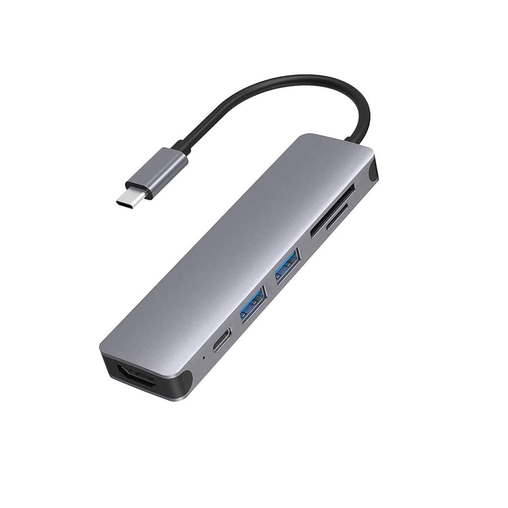 Ein silberner USB-C-Hub mit mehreren Anschlüssen, einschließlich USB, HDMI und SD-Kartensteckplätzen, verbunden durch ein schwarzes Kabel. Der Hintergrund ist weiß.