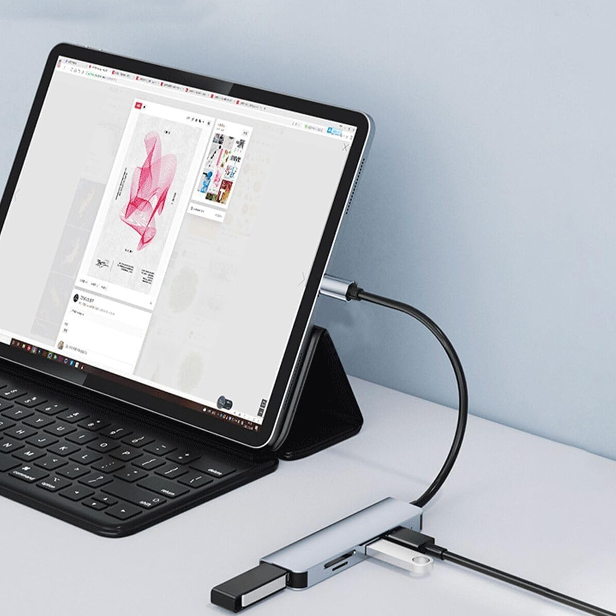 Tablet mit Tastatur und angeschlossenem Hub. Der Bildschirm zeigt eine Webseite an. Es steht auf einem weißen Schreibtisch mit blauer Wand.