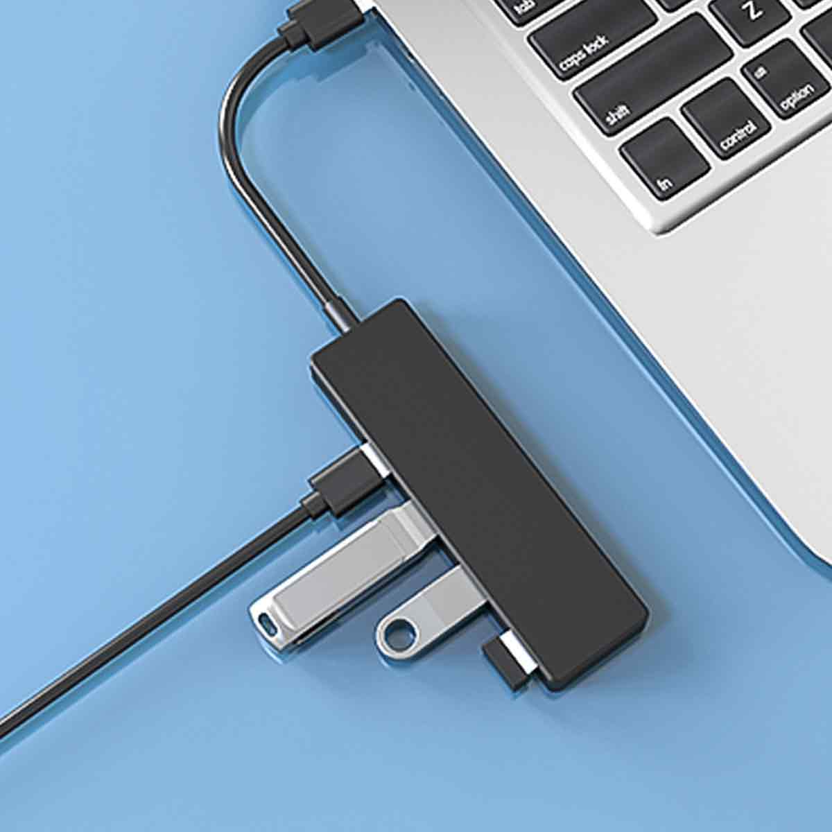Schwarzer USB-Hub mit zwei silbernen USB-Laufwerken, die an einen Laptop auf einer blauen Oberfläche angeschlossen sind.