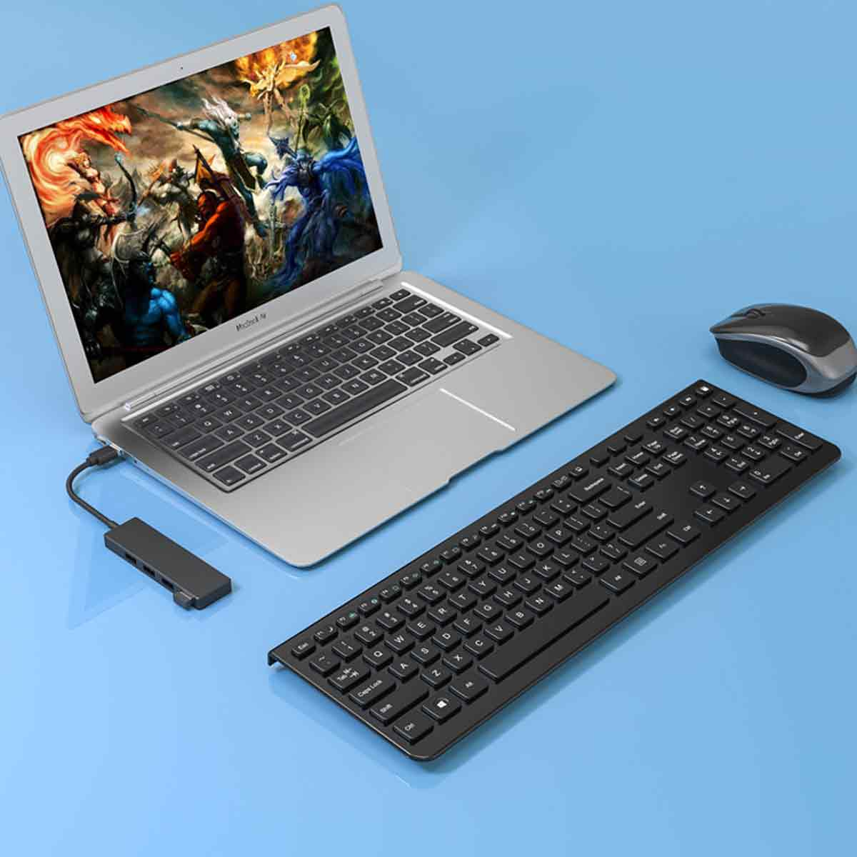 Ein Laptop mit Spiel, eine schwarze Tastatur, eine Maus und ein USB-Hub liegen auf blauer Oberfläche.
