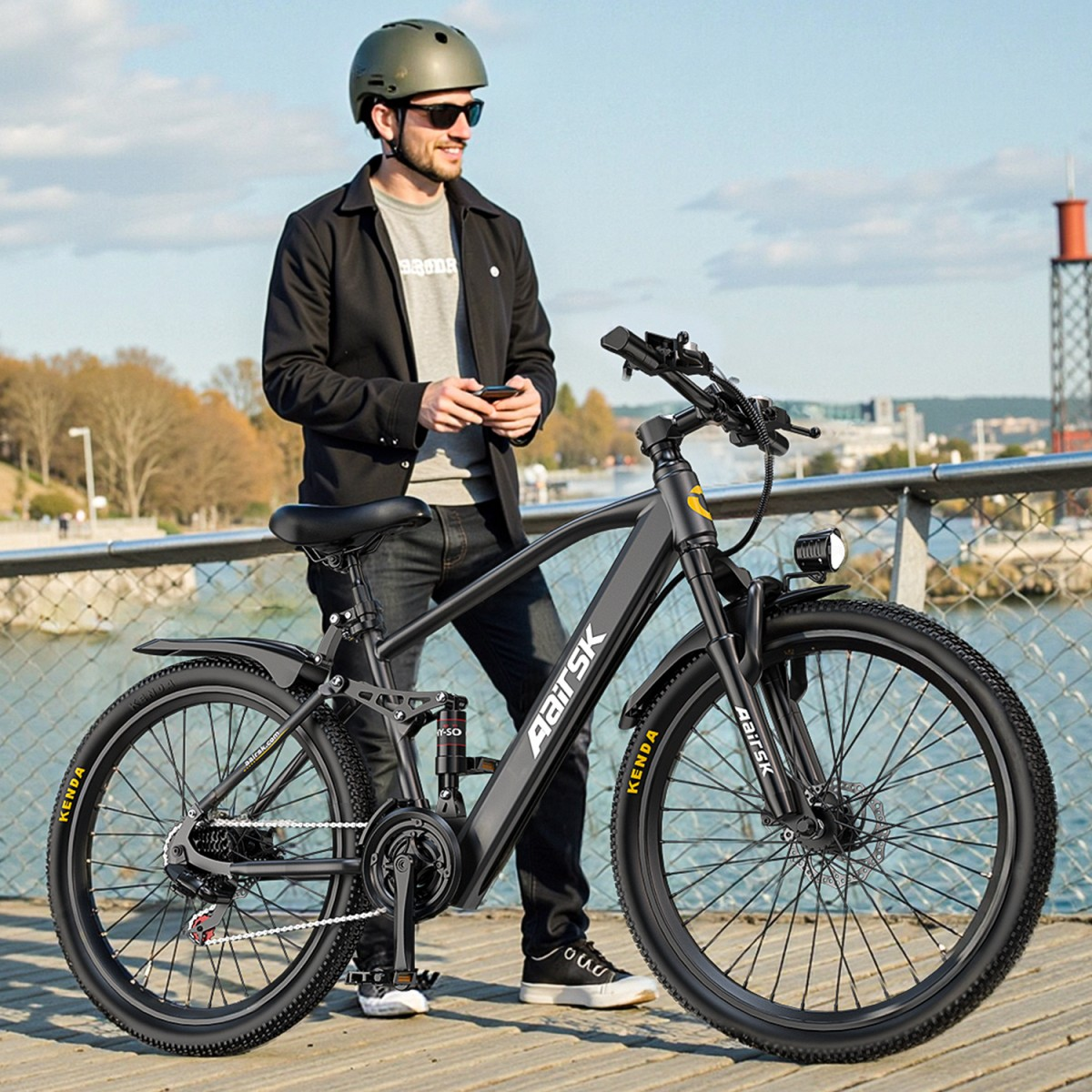 Mann mit Helm steht neben einem schwarzen Elektrofahrrad. Er hält ein Telefon. Im Hintergrund Wasser, Stadt und eine Brücke.